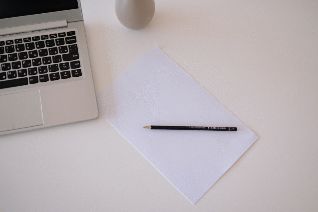 Clean desk surface with a laptop, blank sheet of paper, and pen visible.