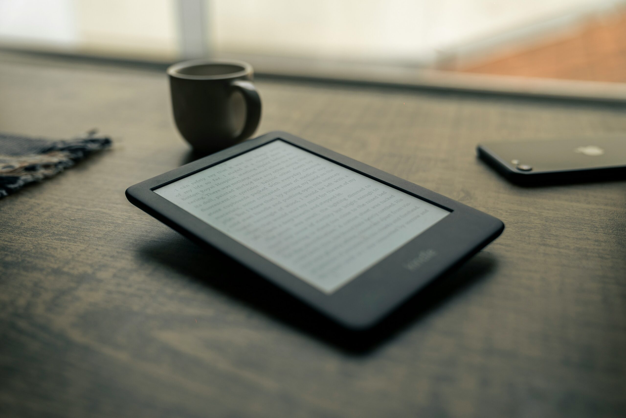 A tablet, phone, and coffee cup on a wooden table.