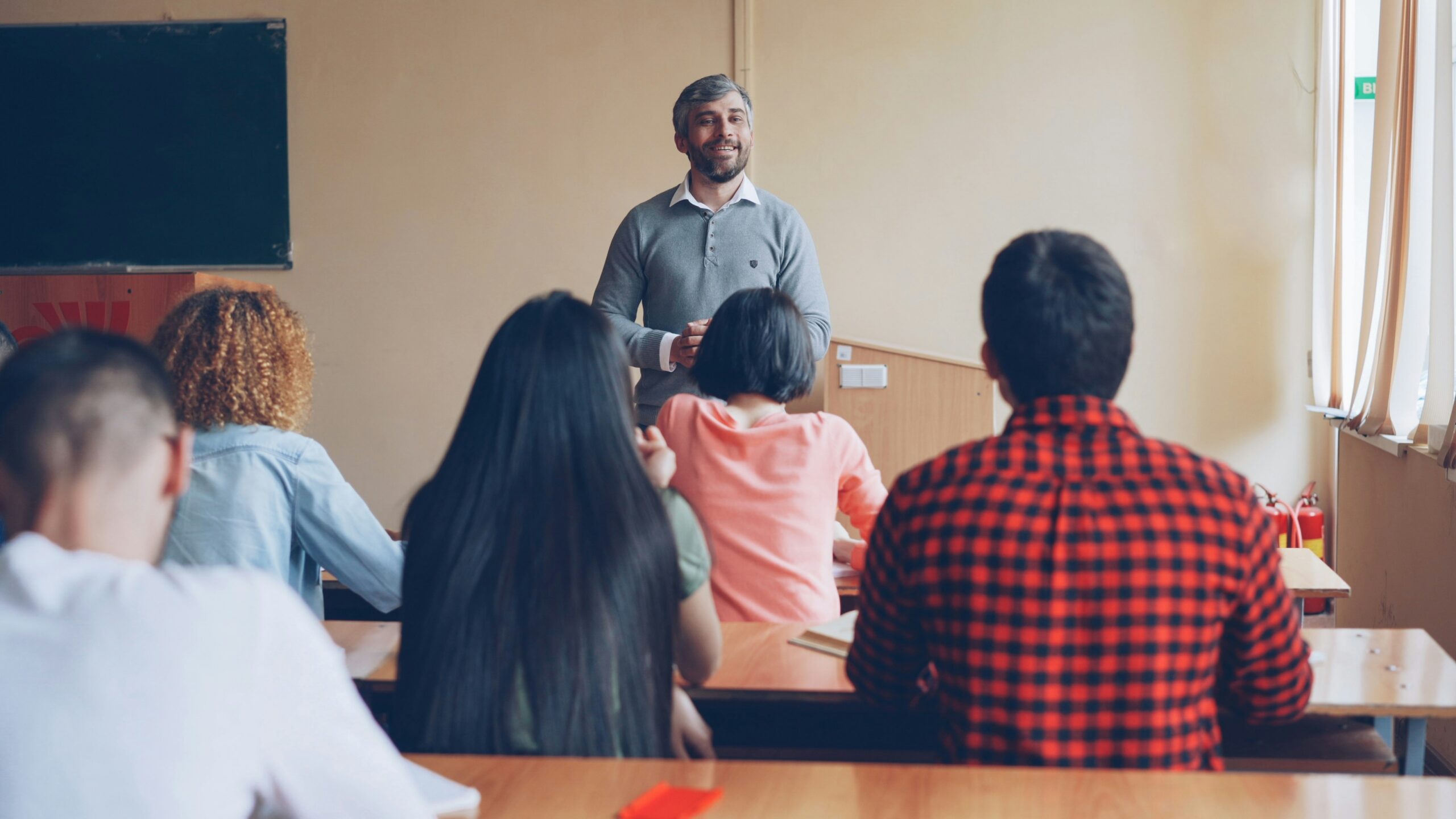 College instructor speaking to a group of students sitting in rows in a classroom.