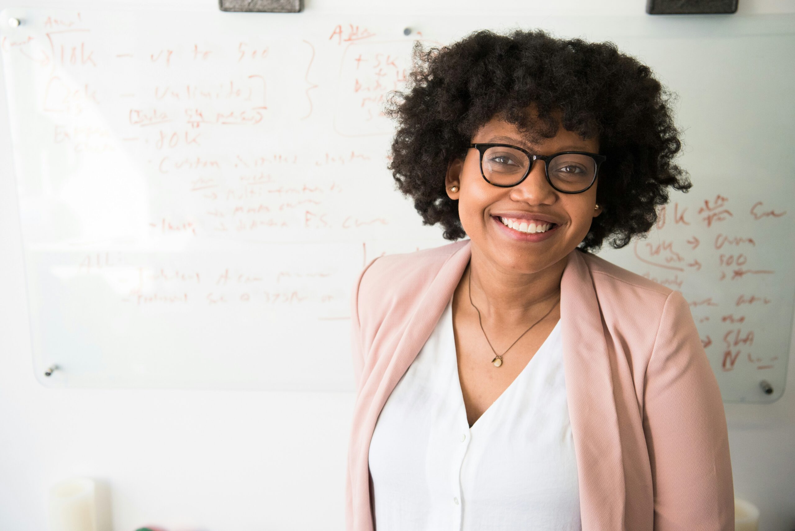 Smiling professor wearing a white shirt, taupe jacket, and glasses.