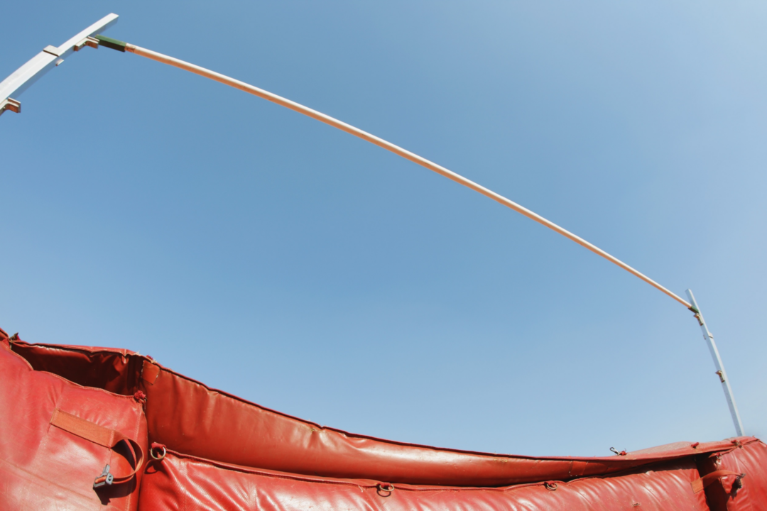 A high jump bar with a red mat set against blue sky.